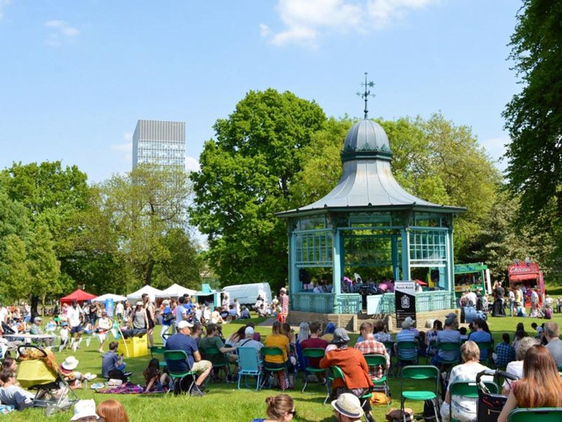 Crowds of people sit on chairs around the bandstand in Weston Park